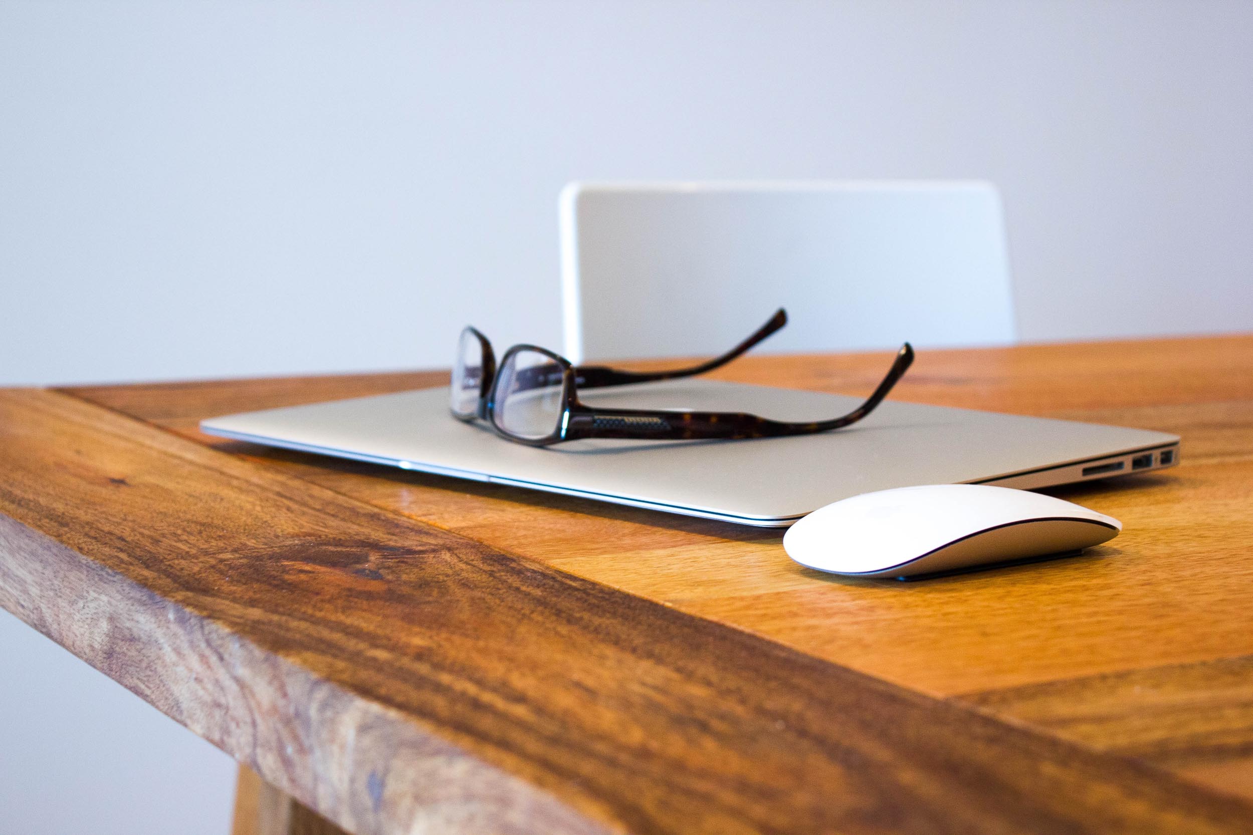 Laptop, mouse and reading glasses placed on a desk